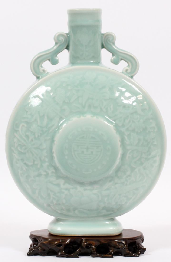 CHINESE CELADON PORCELAIN MOON FLASK: CHINESE CELADON PORCELAIN MOON FLASK, H 13.25", L 9.5" Decorated with symbols of twelve Buddha and a longevity symbol in the center. Accompanied by a wood base.