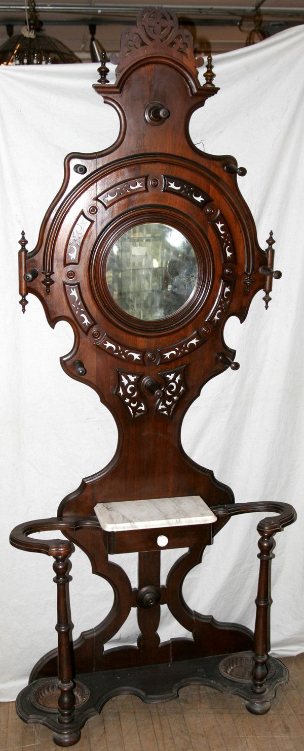VICTORIAN WALNUT HALL TREE, C.1880, H97" W41": VICTORIAN WALNUT HALL TREE, C. 1880, H 97", W 41":Having 2 iron umbrella pans at the base, a center marble top atop one small drawer, 9 pegs for hanging coats, and a circular mirror in the back panel.