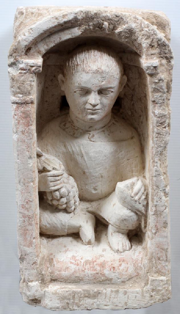 LIMESTONE STELE OF A CHILD ROMAN PERIOD FROM EGYPT: LIMESTONE STELE OF A CHILD, ROMAN PERIOD FROM EGYPT, H 22", W 11", D 7 1/2" :Seated child in niche wearing necklace, holding bunch of grapes and dove. Purportedly from the 3rd century A.D.