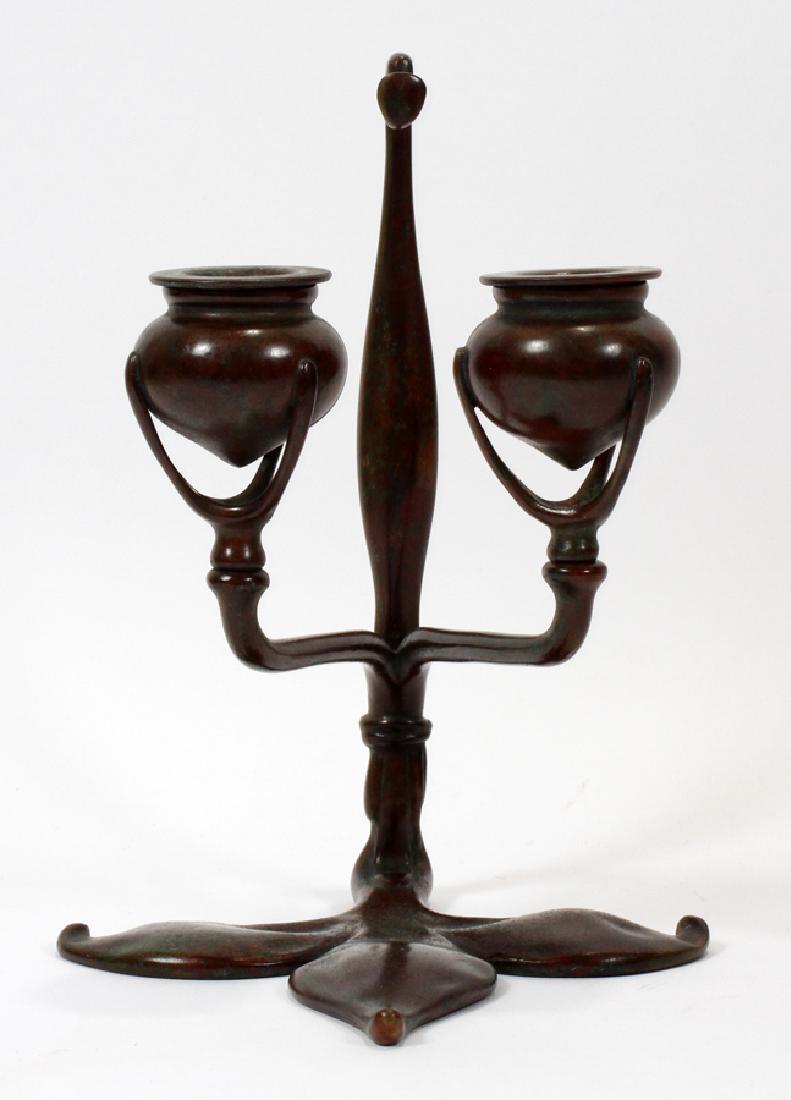 TIFFANY STUDIOS NEW YORK #1232 BRONZE CANDLE STAND: TIFFANY STUDIOS NEW YORK #1232 BRONZE FLEUR DE LIS CANDLE STAND, C. 1910, H 9" D 6" :Impressed trade mark on Fleur de lis base. Two light. Having removable candle cups and green brown patina.