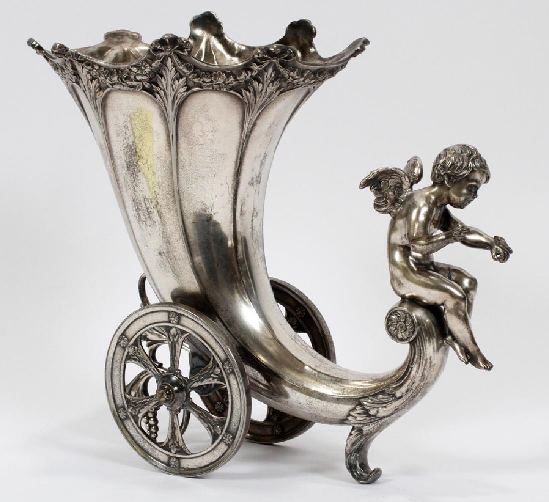 VICTORIAN PLATE DECORATIVE CORNUCOPIA: VICTORIAN PLATE DECORATIVE CORNUCOPIA, H 9 1/2", W 11 1/2", D 4 1/2":A decorative silver tone metal cornucopia. This piece features a chariot style cornucopia equipped with wheels and acanthus leaf mo