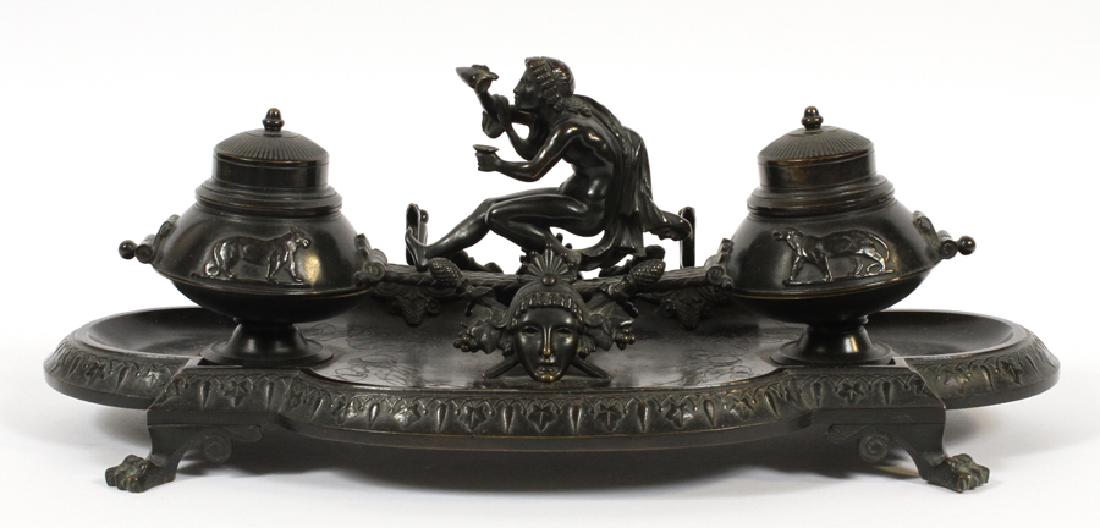 BRONZE INKSTAND MOUNTED WITH DIONYSUS: BRONZE INKSTAND, MOUNTED WITH DIONYSUS GREEK GOD OF WINE 19TH.C. H 7" W 16" Neoclassic ink stand with two wells flank figure of Dionysus pouring wine into goblet. Ink wells are decorated with rampant 