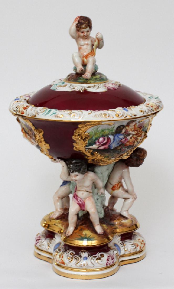 ITALIAN CAPODIMONTE CERAMIC COMPOTE: ITALIAN CAPODIMONTE CERAMIC COMPOTE, H 22", DIA 14"An Italian Capodimonte lidded ceramic compote, probably from the mid-20th century. The piece is adorned with putti featuring an alizarin crimson and