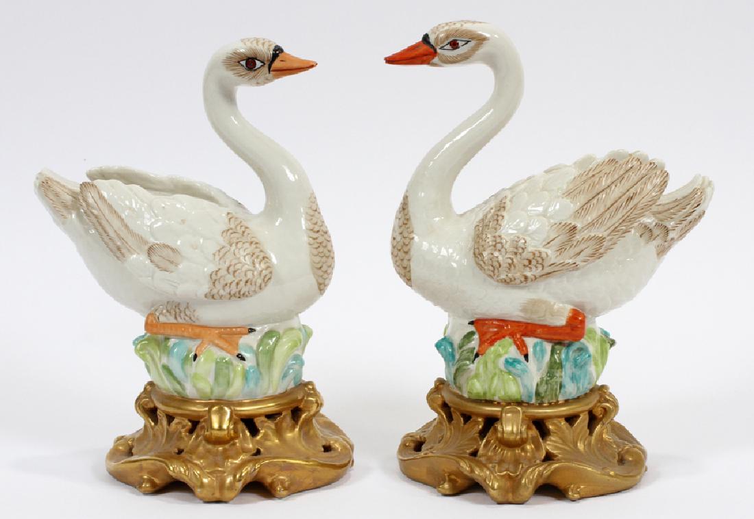 MOTTAHEDEH PORCELAIN SWANS, PAIR: MOTTAHEDEH PORCELAIN SWANS, PAIR, H 8.5", W 6", D 4.5":A pair of Mottahedeh porcelain swan figurines. Each hand-painted piece features a stylized swan atop a scroll form gilt base. Maker's marks to th