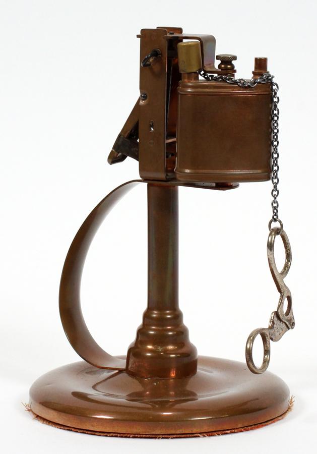 ARTS & CRAFTS, COPPER CIGAR CUTTER, LIGHTER/LAMP: ARTS & CRAFTS, COPPER CIGAR CUTTER, LIGHTER/LAMP, C1930, H 7 1/2" A lighter/lamp mounted on a pedestal with handle and sitting on an integral round base. The plated metal cutter is suspended on a plat