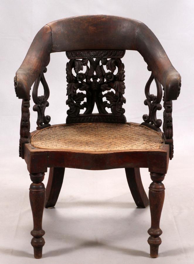 BRITISH COLONIAL CARVED ARM CHAIR: BRITISH COLONIAL CARVED ARM CHAIR, H 35", W 25", L 24" A British colonial carved armchair from Burma. Having and elaborately carved back slat and side slats with a caned seat. Carved wood armrests cur