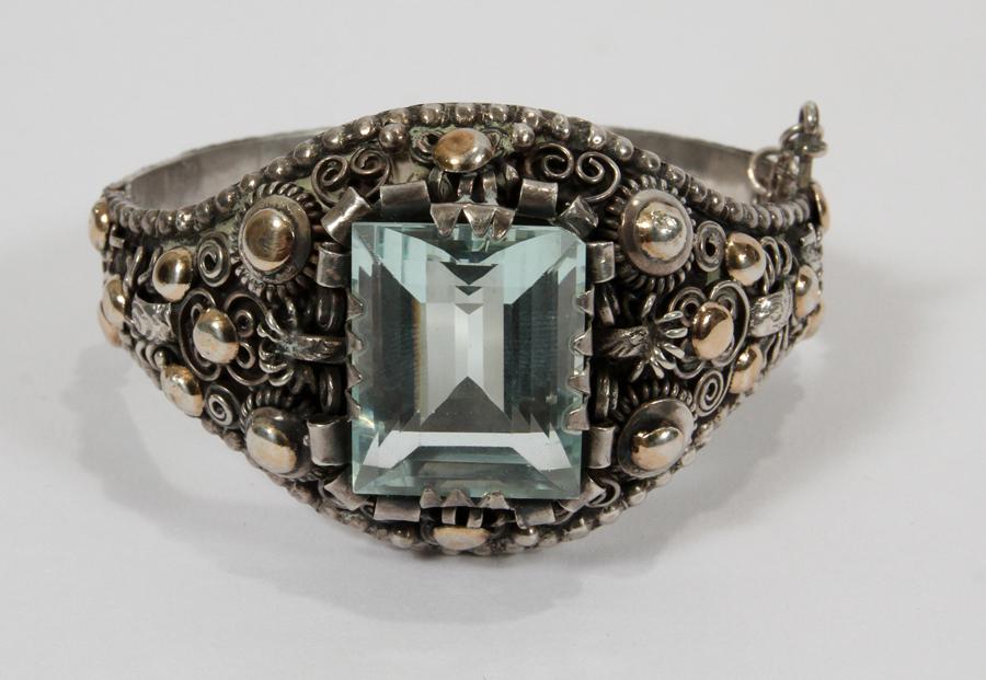EMERALD CUT BLUE CRYSTAL & SILVER CUFF BRACELET: ARGENTINIAN EMERLD CUT BLUE CRYSTAL AND .800 SILVER CUFF BRACELET, W 1.5" TO 0.5" L 7.0" Fruit & floral design with gilt highlights; 1.66 troy ozs. total weight (includes the blue crystal).