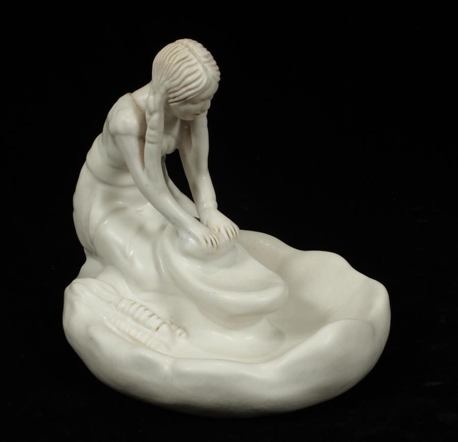 VAN BRIGGLE ART POTTERY FIGURINE: VAN BRIGGLE ART POTTERY FIGURINE, H 6", MAIDEN GRINDING CORN A Van Briggle art pottery figurine. Depicting a Native American maiden grinding corn. Finished in a cream tone matte glaze. Maker's marks i