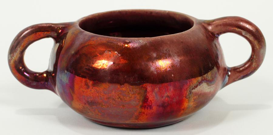 IRA & ELLA PETERS, PEWABIC POTTERY HANDLED VESSEL: IRA & ELLA PETERS, PEWABIC POTTERY HANDLED VESSEL, H 2", W 5", D 3.5"A Pewabic Pottery handled vessel by Ira and Ella Peters. Having a white clay body and drip iridescent glaze boasting oxblood, turqu