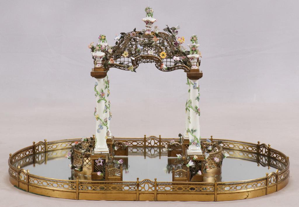 MEISSEN PORCELAIN BRONZE PLATEAU CENTERPIECE: MEISSEN PORCELAIN, BRONZE SURTOUT DE TABLE PLATEAU MIRROR CENTERPIECE H 20" W 21" L 32" A detailed porcelain centerpiece in the form of a floral pergola. Resting on a plateau mirror centerpiece.
