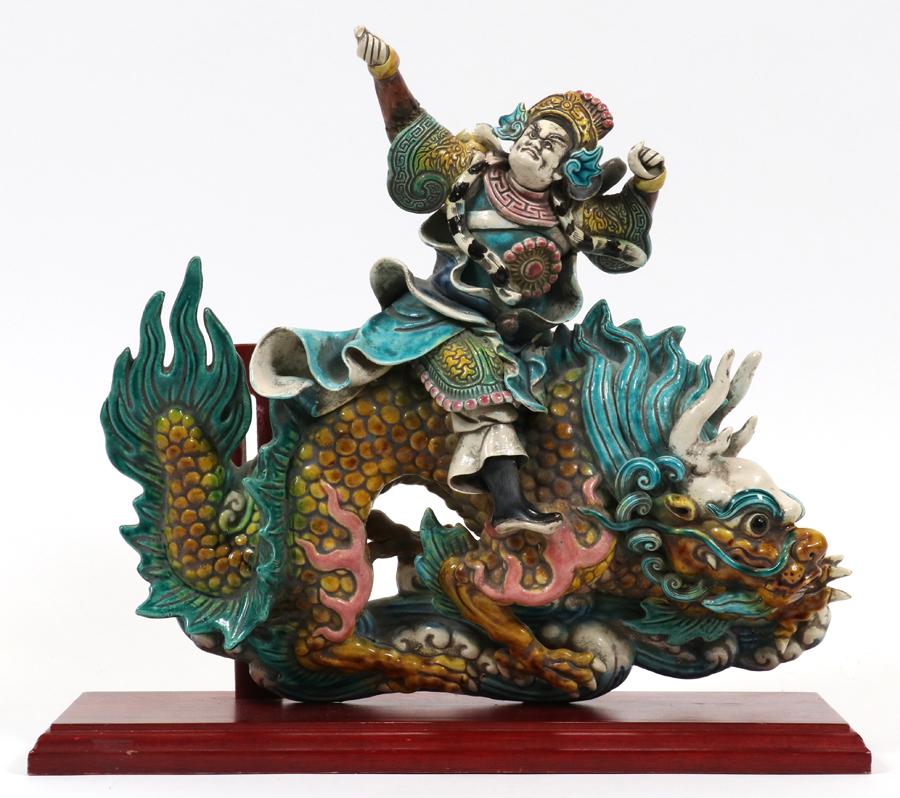 CHINESE POTTERY ROOF TILE, H 13.25", W 14": CHINESE POTTERY ROOF TILE, H 13.25", W 14" A pottery roof tile depicting a Chinese warrior riding on the back of a dragon. Mounted on a wood stand. The tile is signed, It has an impressed signature at
