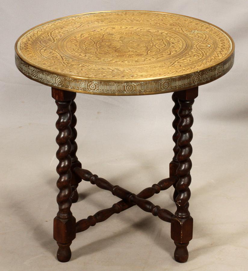 MIDDLE EASTERN STYLE BRASS TRAY TABLE: MIDDLE EASTERN STYLE, BRASS TRAY TABLE ON A WOODEN BASE, H 22", DIA 23" The tray is etched brass laid over a wooden frame. The tray sits on a folding, oak wood base with turned legs. The base was made