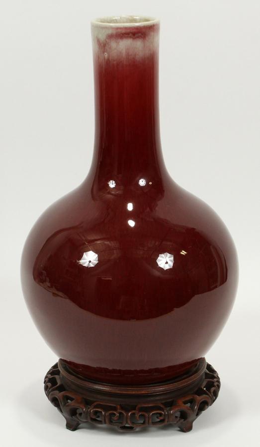 CHINESE PORCELAIN SANG DE BOEUF PORCELAIN VASE: CHINESE PORCELAIN SANG DE BOEUF PORCELAIN VASE, H 14" DIA 8 1/2" Of globular form with a tall neck; deep red glaze with a cream glaze at the rim. No bottom mark; pierced wood stand. Provenance: Doyles