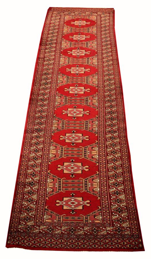 PAKISTAN, BOKHARA HAND WOVEN WOOL RUG: PAKISTAN, BOKHARA HAND WOVEN WOOL RUG, W 2' 7", L 10' 8" Having a red ground, three borders, and nine equally spaced geometric medallions along the field.
