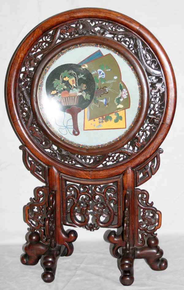 CHINESE CLOISONNÉ AND CARVED TEAKWOOD SCREEN: CHINESE CLOISONNÉ AND CARVED TEAKWOOD SCREEN, H 30", L 19":Having a carved wood stand and pierced dragon design bordering an inset cloisonné charger in a fan motif. Circa 1930 From the Estate of Rob