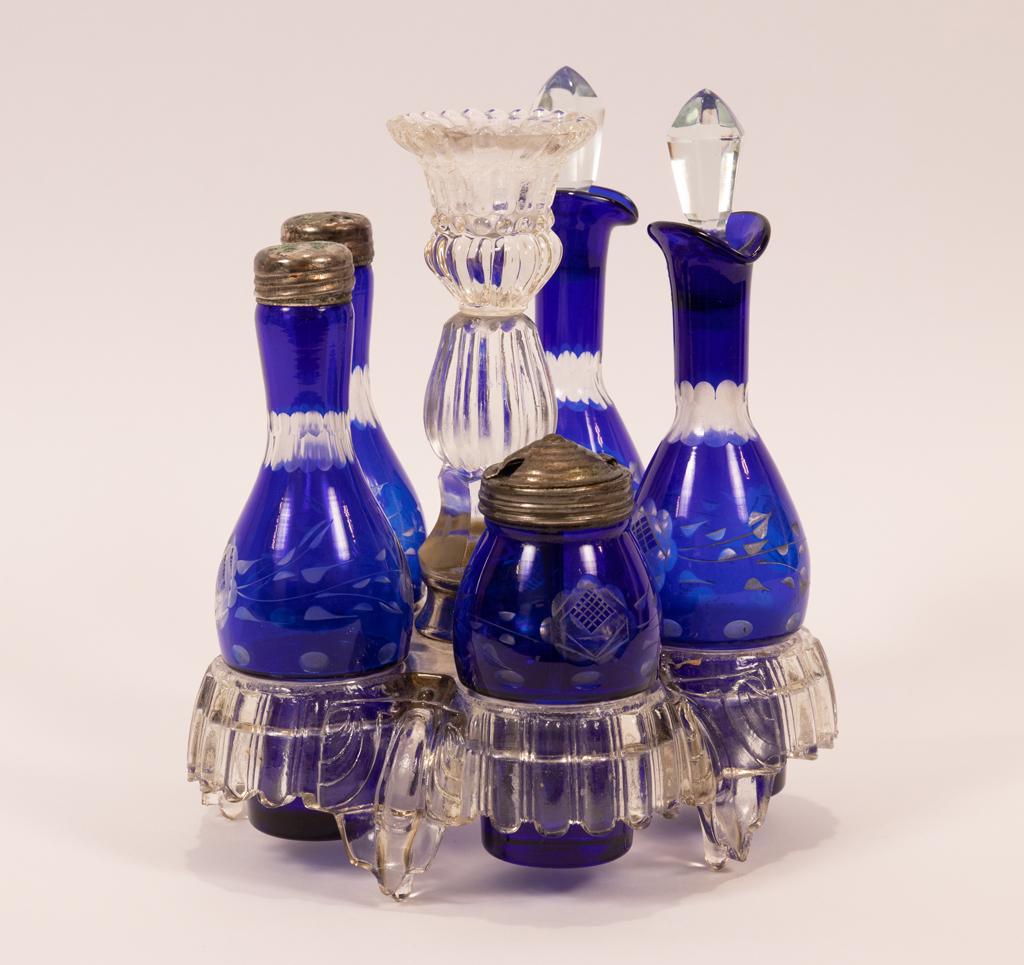 COBALT GLASS CONDIMENT SET IN STAND C 1880 H 9": COBALT GLASS CONDIMENT SET IN STAND C 1880 H 9" 5 cobalt blue accented condiment bottles: salt , perpper, mustard, vinegar, oil bottles in plain clear glass holder with center candlestick.