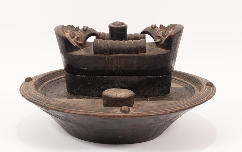 AFRICAN CARVED WOOD PLAQUE, CENTER BOX FOR NUTS 19TH.C.: AFRICAN CARVED WOOD PLAQUE, CENTER BOX FOR NUTS 19TH.C. D 6" DIA 15.5" Double stylized heads carved on cover of central box. # T 2010 #5229. Estate of Jack Faxon, Birmingham, MI.