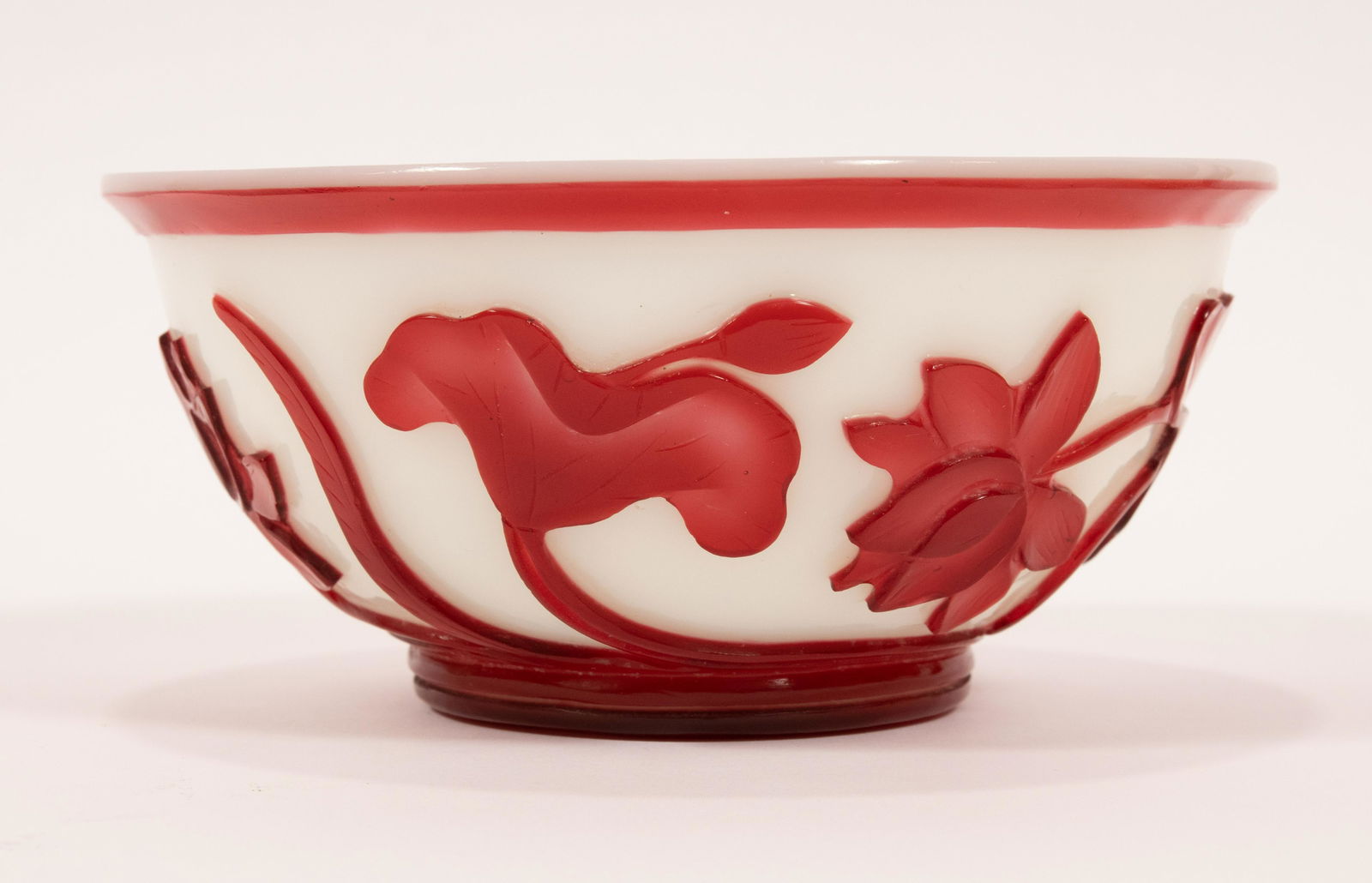 CHINESE GLASS RED BOWL WITH WHITE GROUND DIA 5.75": CHINESE GLASS RED BOWL WITH WHITE GROUND DIA 5.75" Depicting a floral motif with a swirl design on the underside. Provenance: Estate of Jack Faxon, Michigan Senator, and creator of the Michigan Counci