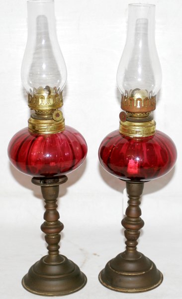 CRANBERRY GLASS & BRASS PEG LAMPS, C. 1860,: CRANBERRY GLASS & BRASS PEG LAMPS, C. 1860, PAIR, H 14" OVERALL:Each having a clear glass chimney, cranberry glass font, and brass base. From the estate of Rose Bauer, Brooklyn Mi.