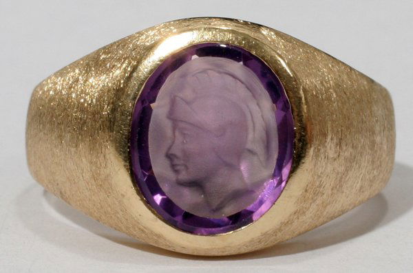 GENTS 14KT. Y/GOLD AND AMETHYST INTAGLIO RING: GENTS 14KT. YELLOW GOLD AND AMETHYST INTAGLIO RING:The domed ring is bezel set with a 12.00 X 9.70mm oval amethyst intaglio (featuring a warrior's head in profile and a faceted pavilion) which is medi