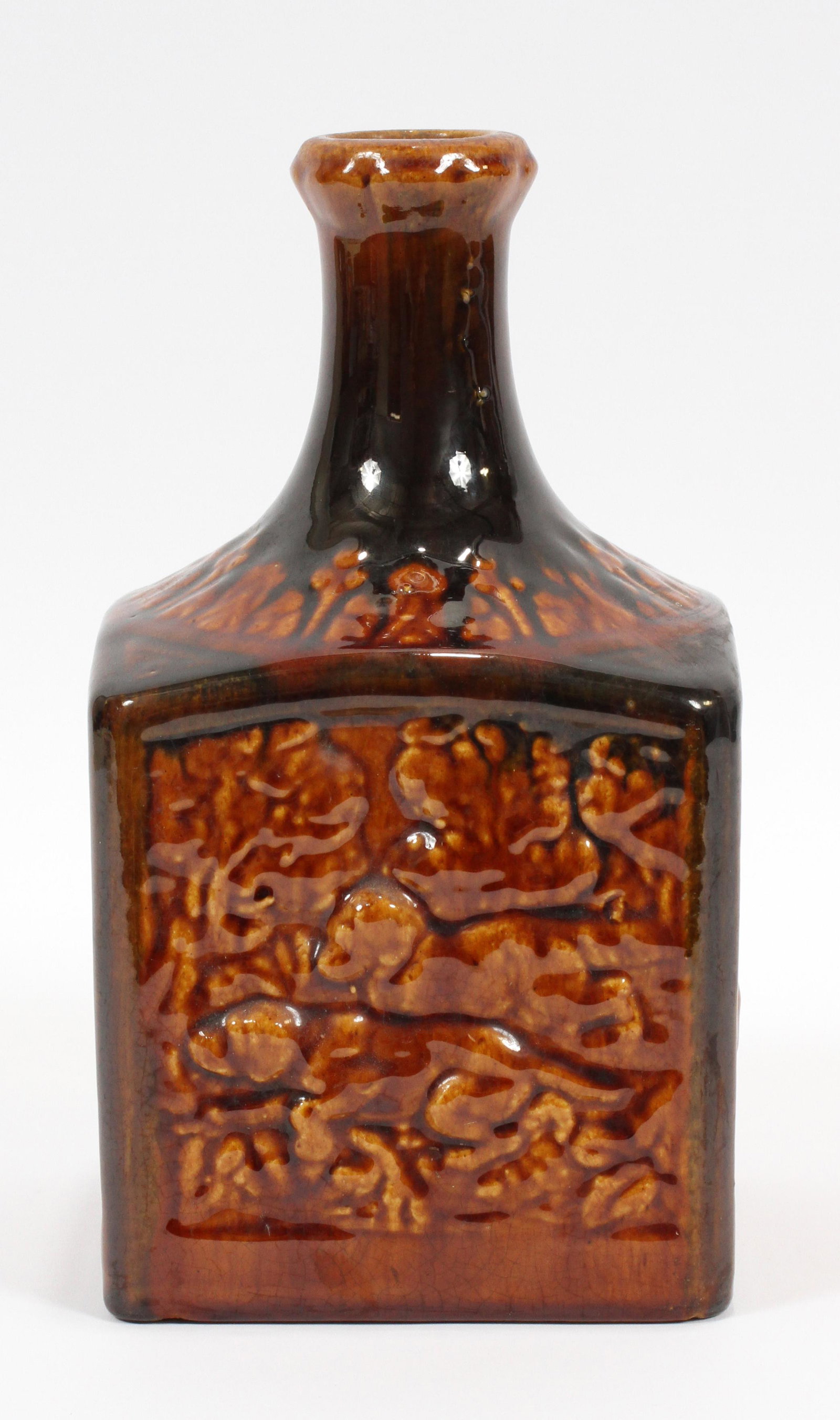 CERAMIC BOTTLE BOTTLE FORM MUSIC BOX, H 9.5", W 5", D: CERAMIC BOTTLE BOTTLE FORM MUSIC BOX, H 9.5", W 5", D 5"A ceramic music box. This piece offers a ceramic decanter with a glossy, umber glaze with a music box in the bodice. Features four panels of hun