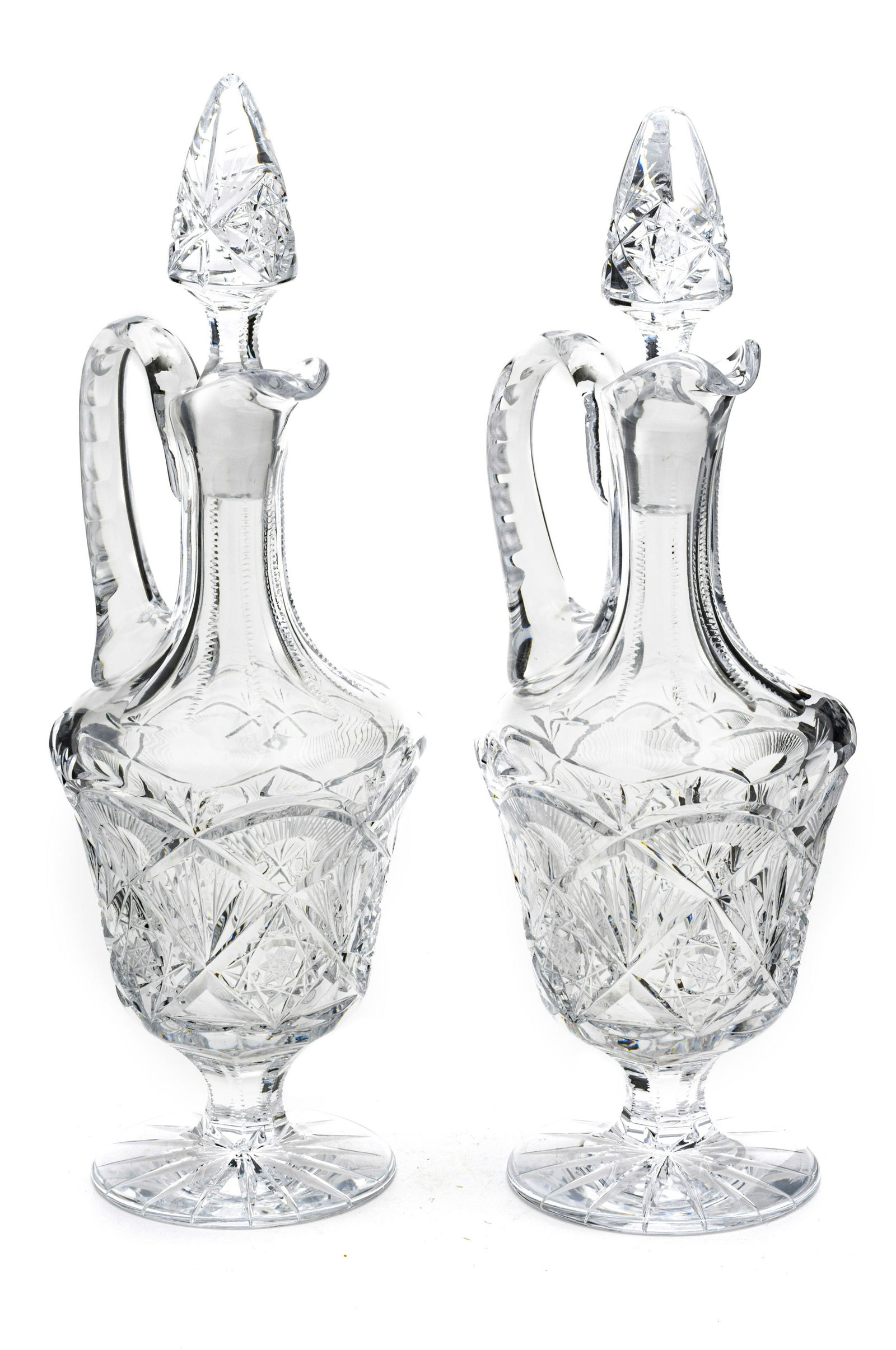 CUT GLASS WINE DECANTERS, PAIR H 14,5": CUT GLASS WINE DECANTERS, PAIR H 14,5" Cruet shape with pedestal bases, handles, stoppers. Hand cut. From the estate of Lois Jacobs, Grosse Pointe Shores.