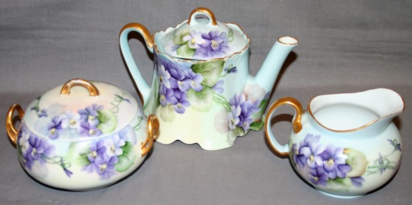 BAVARIAN HAND PAINTED PORCELAIN TEA SET, THREE : BAVARIAN HAND PAINTED PORCELAIN TEA SET, EARLY 20TH CENTURY, THREE PIECES, H 4" - 5":Including 1 creamer, 1 covered sugar bowl and 1 teapot. All are hand painted with purple floral motifs and fired go