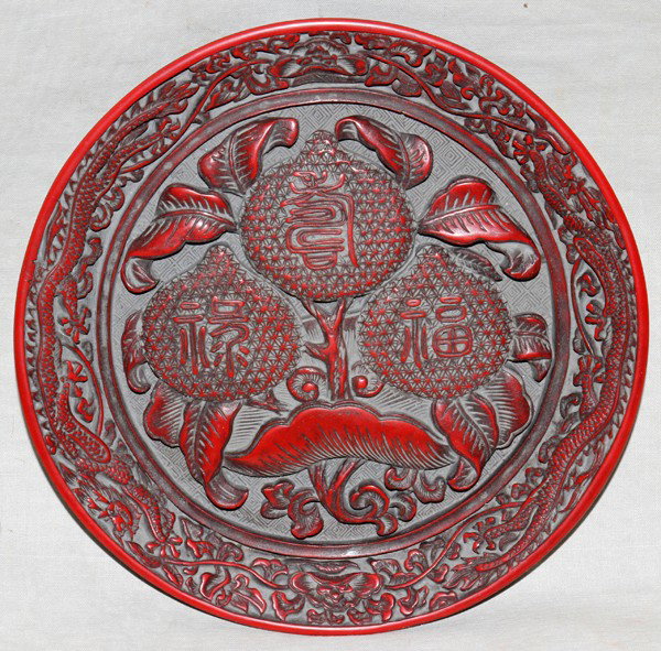 CHINESE CINNABAR PLATE, H 1", DIA 7 5/8": CHINESE CINNABAR PLATE, H 1", DIA 7 5/8":Floral and dragon forms and symbols for happiness, longevity and wealth all in relief. Characters on underside.