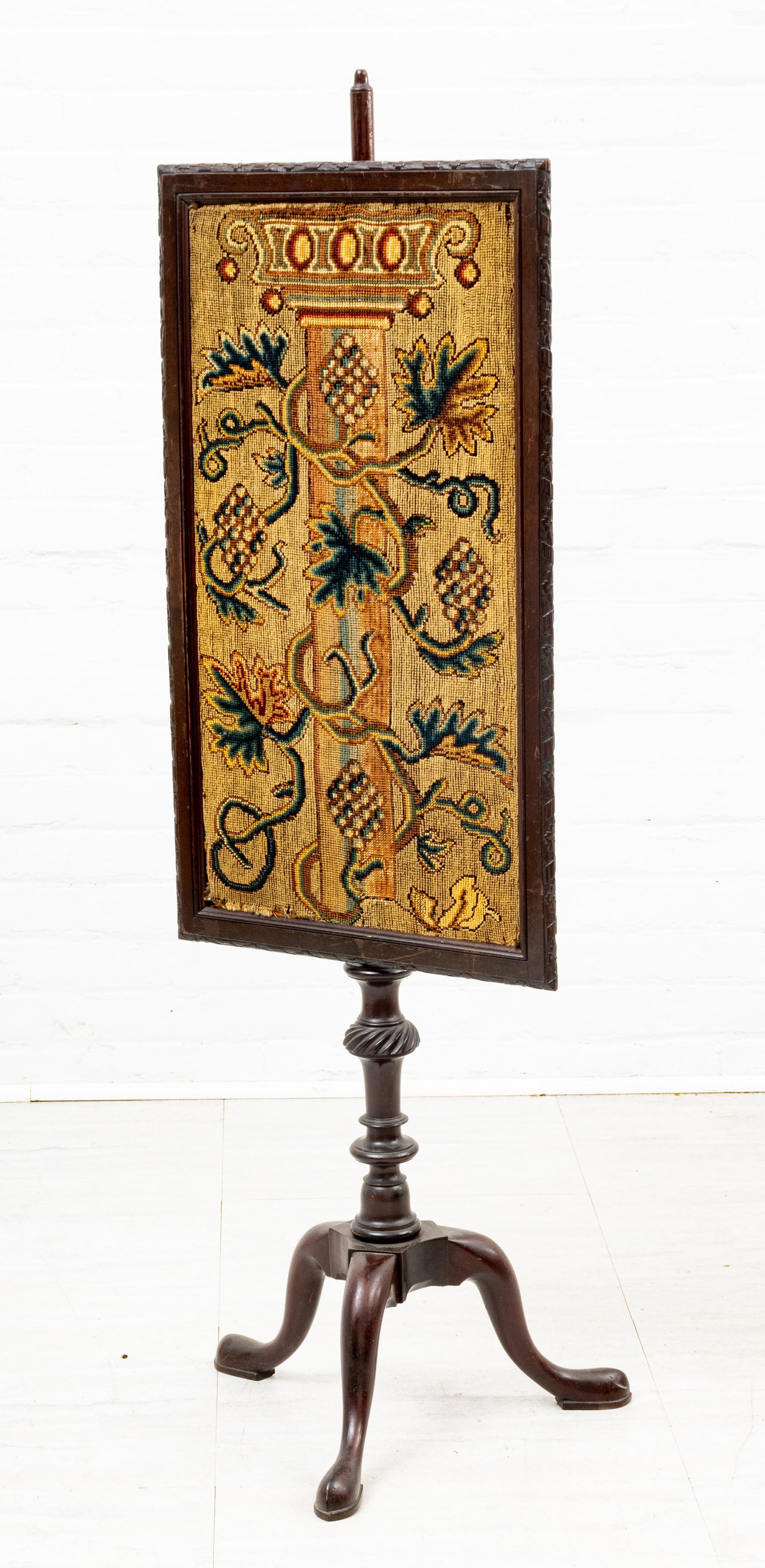 MAHOGANY AND NEEDLEPOINT FIREPLACE SCREEN H 53" W 17" D 19": MAHOGANY AND NEEDLEPOINT FIREPLACE SCREEN H 53" W 17" D 19" Needlepoint screen depicting a central column with grapes and vines. Having a mahogany frame set on a mahogany tripod stand.