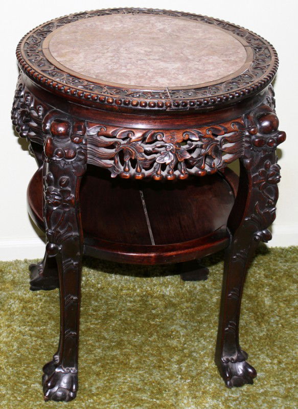 CHINESE TEAKWOOD STAND, C. 1900, H 26", DIA 19": CHINESE TEAKWOOD STAND, C. 1900, H 26", DIA 19":Inset rouge marble top, carved apron and supports joined by a shelf stretcher. From the Estate of Pearl McKenney, Grosse Pointe Farms.