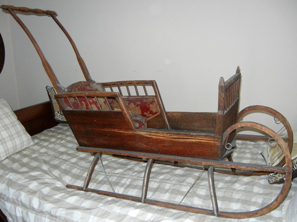 WOOD CHILD'S SLED, W 19", L 55": WOOD CHILD'S SLED, W 19", L 55":cutter sled with turned spindle and bent wood push handle, metal supports and wood construction with a red and beige seat; dowel trim to sides of seat and front bulkhea