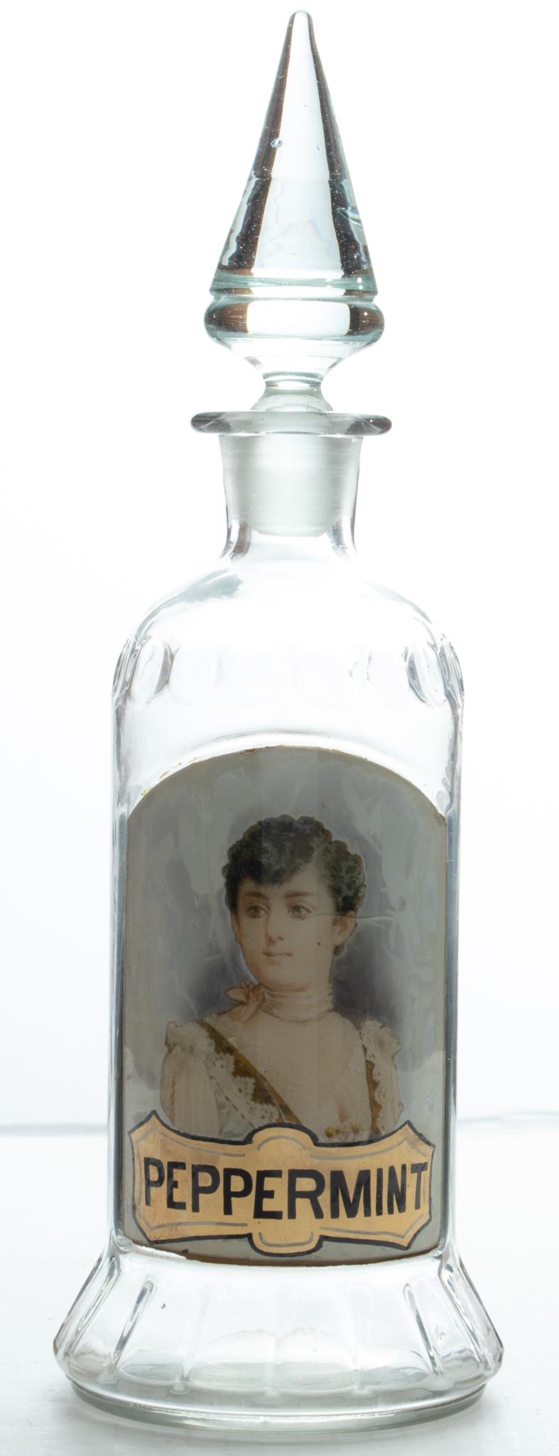 BOTTLE WITH GLASS LABEL "PEPPERMINT", H 13": BOTTLE WITH GLASS LABEL "PEPPERMINT", H 13" Spear form glass stopper. Hand blown. Transfer print image. Possibly for counter top display.