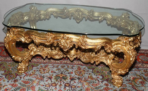 CARVED & GILT WOOD COFFEE TABLE, H 20", L 49",: ROCOCO STYLE CARVED & GILT WOOD COFFEE TABLE, H 20", L 49", D 29":Having a glass top and an ostentatious carved and gilt wood base.