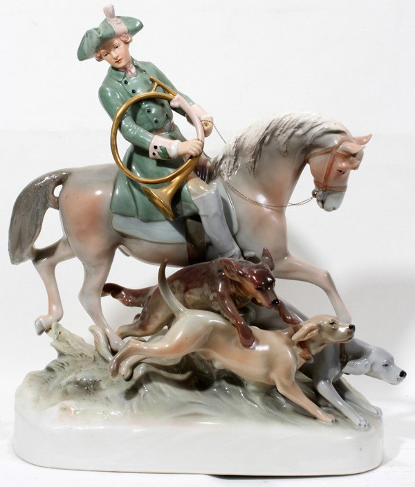 ROYAL DUX PORCELAIN EQUESTRIAN FIGURE H 19 1/4": ROYAL DUX PORCELAIN EQUESTRIAN FIGURE, H 19 1/4", L 16":Featuring a hunter riding a horse with a horn in one hand and three dogs at the base. Measures H.19 1/4" x 16" x 9".