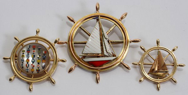 14 KT YELLOW GOLD NAUTICAL BROOCHES, THREE,: 14 KT YELLOW GOLD NAUTICAL BROOCHES, THREE, DIA 1" - 2":Each is in the form of a ship's wheel, two contain a sailboat and the other nautical flags. All are stamped "14K". Totaling approximately 33.6 g