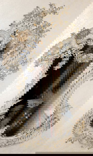 092129: CARVED WOOD & GESSO FRAMED MIRROR: HAND CARVED WOOD AND GESSO FRAMED MIRROR, C. 1930, H 64", W 38":Hand painted floral and leaf designs on sides, carved head on lower part of frame. Carved putti on top left of mirror. Shell carved desi