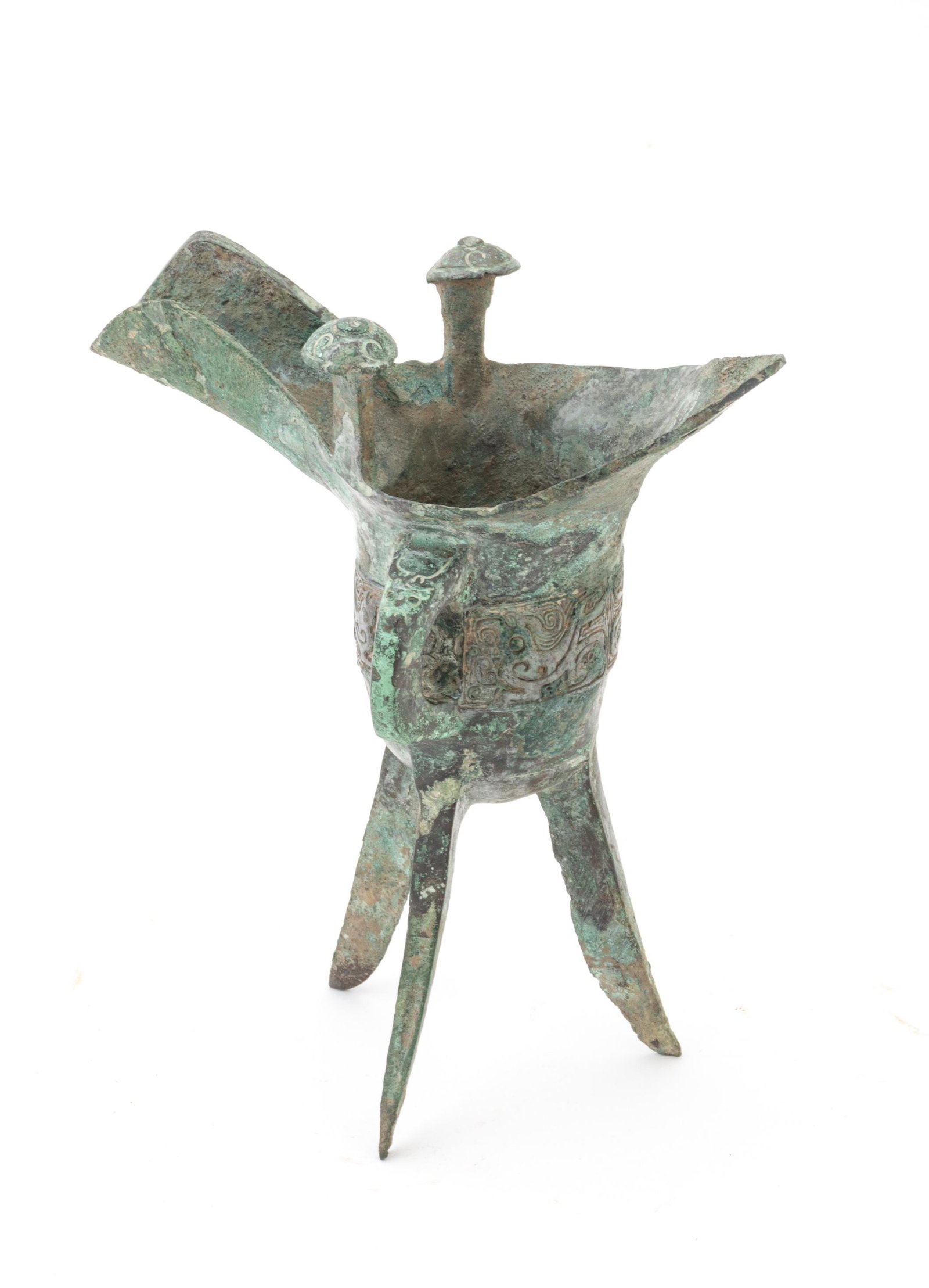Chinese Archaic Bronze Wine Vessel, Shang Dynasty, H 7.5'' W 3.75'' L 6.5'' 490g: Chinese Archaic Bronze Wine Vessel, Shang Dynasty, H 7.5'' W 3.75'' L 6.5'' 490g | An archaic Chinese bronze wine vessel. Presented on three spay legs. With a band of motifs on the perimeter of the ba