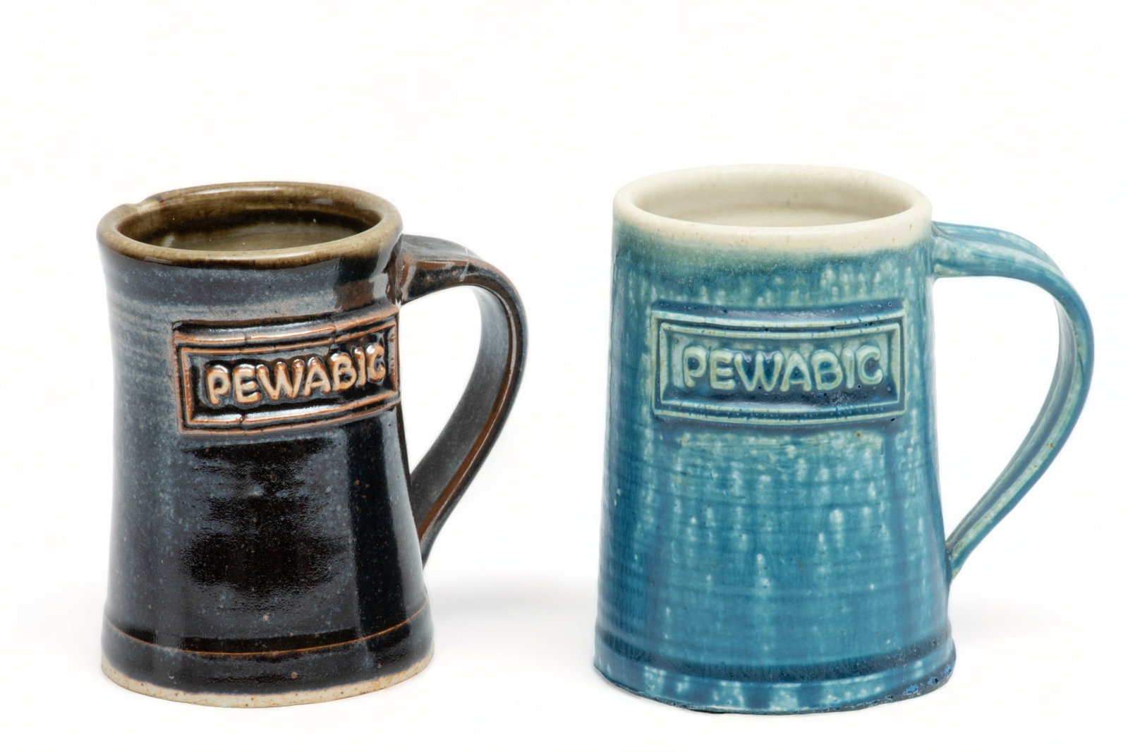 Pewabic Pottery (Detroit, Est. 1903) Handled 'PEWABIC' Mugs, Ca. 1980, H 5" W 3.75" L 4.75" 2 pcs: Pewabic Pottery (Detroit, Est. 1903) Handled 'PEWABIC' Mugs, Ca. 1980, H 5" W 3.75" L 4.75" 2 pcs | the mugs are rendered in the Pewabic Blue and Gun Metal glazes. Each bearing signature branding to t