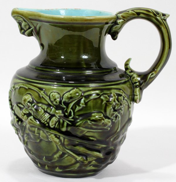 SARREGUEMINES MAJOLICA PITCHER, C. 1890, H 7": SARREGUEMINES MAJOLICA PITCHER, C. 1890, H 7":Having a knight on horseback at one side and a man on a donkey at the other, a mask at the spout, all covered by a moss green glaze. Incised "43" and stam