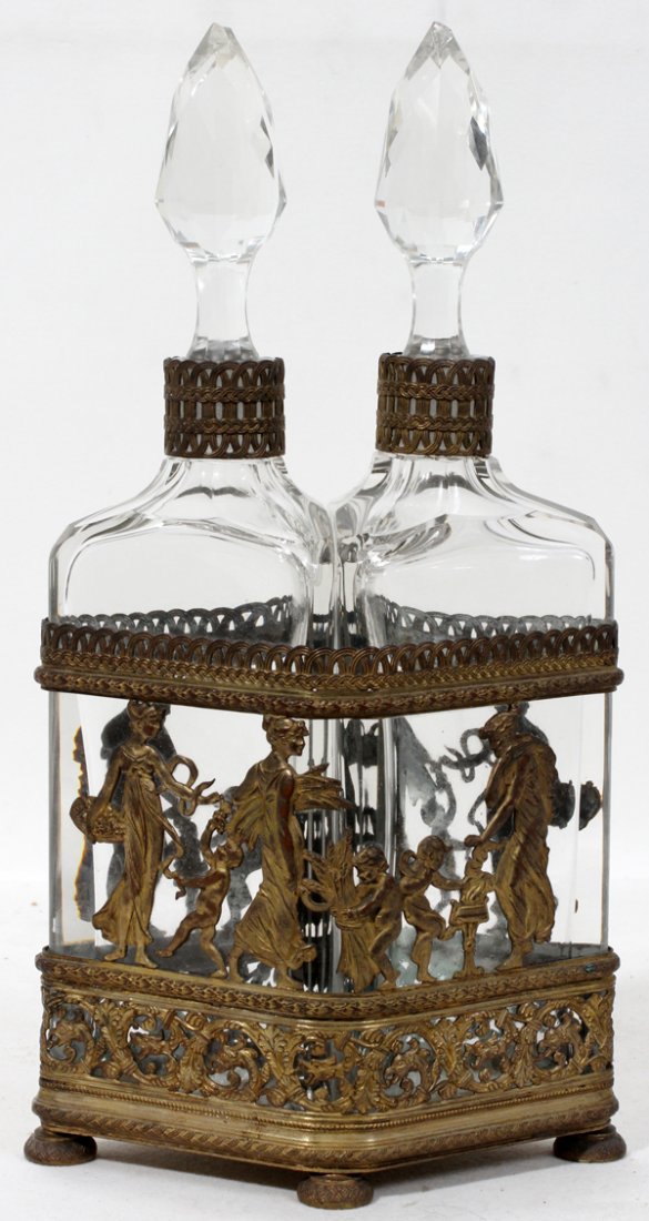 FRENCH CRYSTAL COLOGNE BOTTLES IN A METAL FRAME: FRENCH CRYSTAL COLOGNE BOTTLES (2) IN A GILT METAL FRAME, C. 1920, H 11":Allegorical dancers decorate footed and diamond form metal frame. Circa 1920.