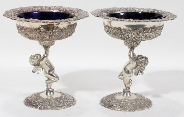 JAPANESE SILVER PLATE FIGURAL COMPOTES, PAIR,: JAPANESE SILVER PLATE SMALL OPEN FIGURAL COMPOTES, PAIR, H 6", DIA 5":With blue glass inserts. A cupid supports each at stem with floral and leaf design. Stamped at the underside with Japanese charact