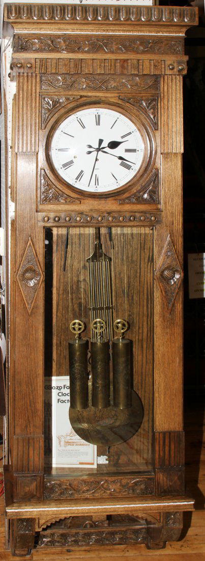 GAZO OAK HANGING WALL CLOCK, H 88", W 24": GAZO OAK HANGING WALL CLOCK, H 88", W 24":Described as a 'Encino' clock, having a crown molding above carved vine designs, white porcelain face inscribed: 'Gazo'; Roman numerals with hour and seconds