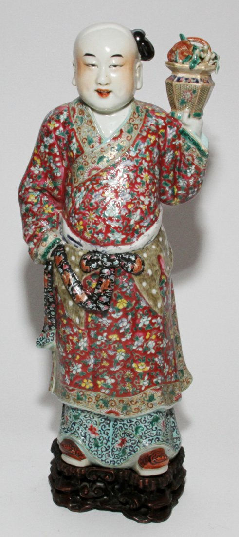 CHINESE PORCELAIN FIGURE OF A MAN, H 17", W 7 1/2": CHINESE PORCELAIN FIGURE OF A MAN, H 17", W 7 1/2":Holding a flowering jardinière in his raised left hand, open mouth shows teeth and pierced ear lobes. Mounted on a teakwood stand.