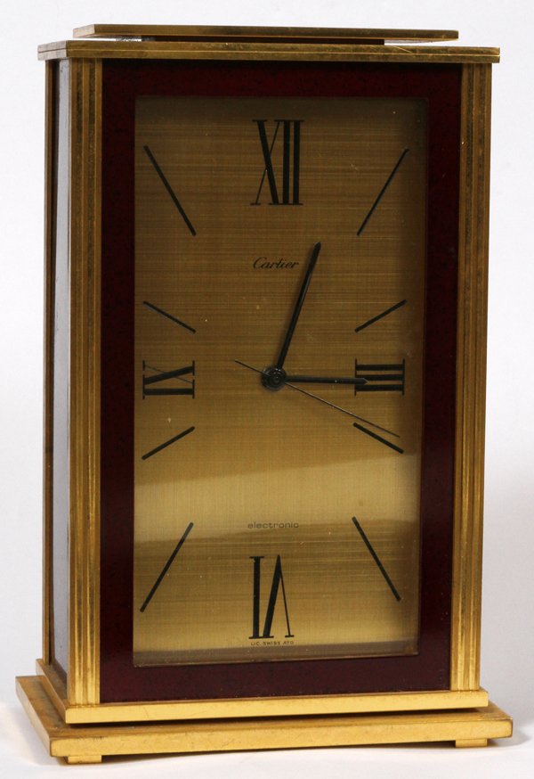 CARTIER DESK CLOCK, H 6 1/2": CARTIER DESK CLOCK, H 6 1/2":Brass case with faux red stone enamel sides and border, brass face with Roman quarter-hour numerals, battery powered quartz movement. Marked "Cartier, Electronic", Swiss m