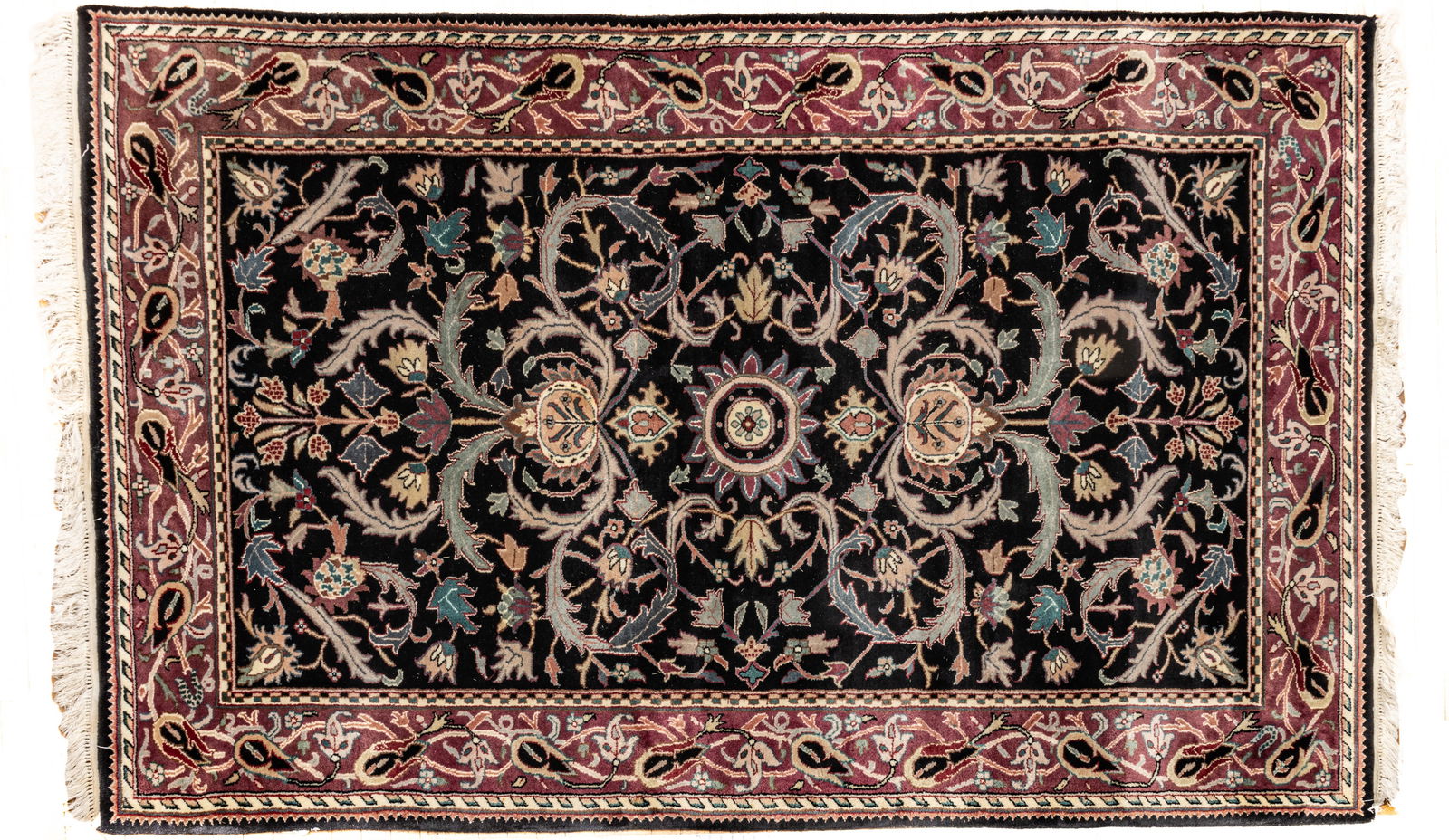Indo-Agra Moghol Handwoven Wool Rug, Ca. 1980-1990, W 5' 7" L 8' 7": Indo-Agra Moghol Handwoven Wool Rug, Ca. 1980-1990, W 5' 7" L 8' 7" Black central field with overall bold floral and leaf designs and a plum colored outer border. Provenance: Property from the