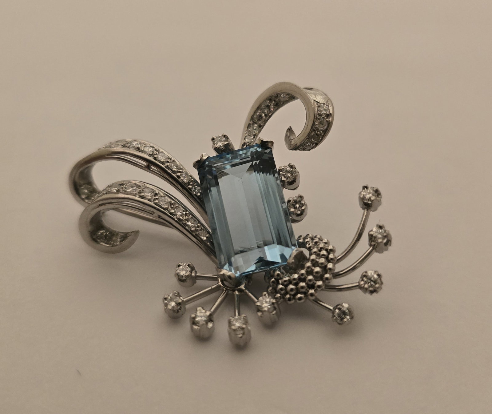 Platinum, 14k White Gold, Topaz and Diamond Brooch L 2" 12.8 g: Platinum, 14k White Gold, Topaz and Diamond Brooch L 2" 12.8 g A hand-fabricated brooch in 14k white gold and platinum having scrolled foliate flourishes with an emerald cut topaz and diamond melee ac