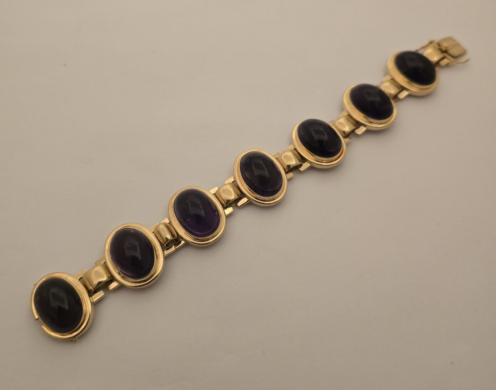 18k Yellow Gold and Amethyst Link Bracelet L 7" 70.2 g: 18k Yellow Gold and Amethyst Link Bracelet L 7" 70.2 g An oval cabochon amethyst link bracelet bezel set in 18k yellow gold having a box clasp with safety catches. Marked 750 18k 374 to the back of cl