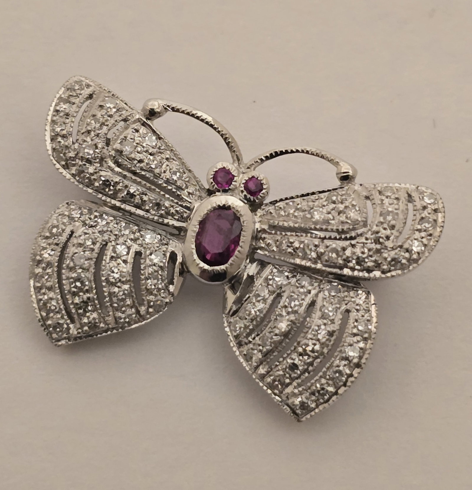 18k White Gold, Ruby, and Diamond Butterfly Pin L 1" 4.6 g: 18k White Gold, Ruby, and Diamond Butterfly Pin L 1" 4.6 g An endearing little butterfly pin set in 18k white gold having allover round, brilliant melee diamond pavé and faceted ruby accents. M