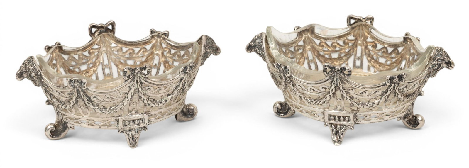German Silver Openwork Crystal Lined, Ca. 1900, H 2.5" W 5.5" L 3.5" 7.49 grams 1 PAIR: German Silver Openwork Crystal Lined, Ca. 1900, H 2.5" W 5.5" L 3.5" 7.49 grams 1 PAIR A pair of pierced footed open bowls with ribbons, swags and a ram's head at either end. Cut glass original fitted