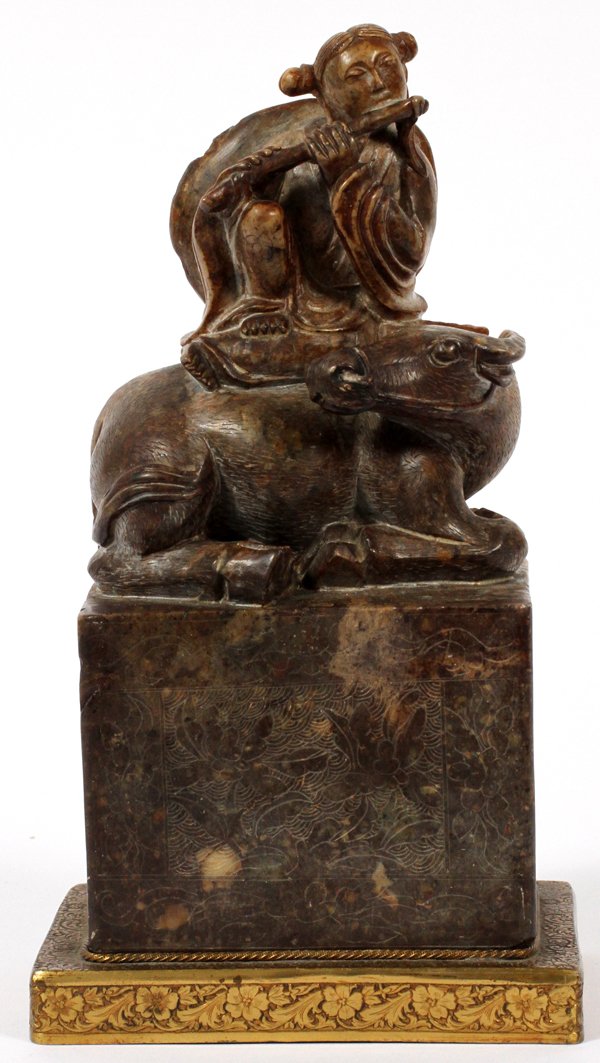 CHINESE CARVED BROWN SOAPSTONE FIGURE ON BUFFALO: CHINESE CARVED BROWN SOAPSTONE FIGURE ON A BUFFALO, H 7 1/2" TOTAL, W 3 5/8":Chased brass or brass plated base.